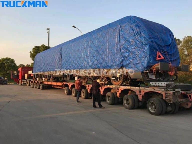 Máquinas industriais de grandes dimensões cobertas com uma lona azul num semirreboque de plataforma baixa