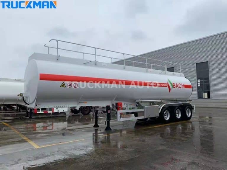 Camião-cisterna branco modernizado, com o logótipo "Dangerous Goods", estacionado na superfície molhada de uma zona industrial.